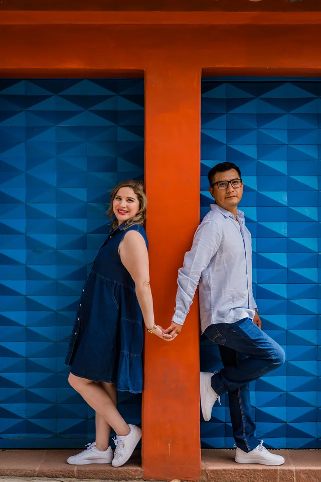 Maria Esthela y Pablo recargados en una columna naranja